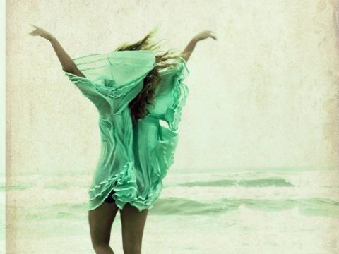 A woman in a flowing mint-green dress leaping on the beach