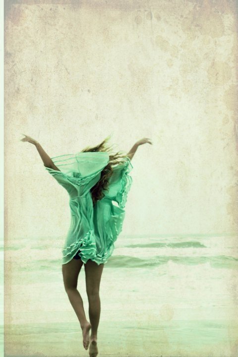 A woman in a flowing mint-green dress leaping on the beach
