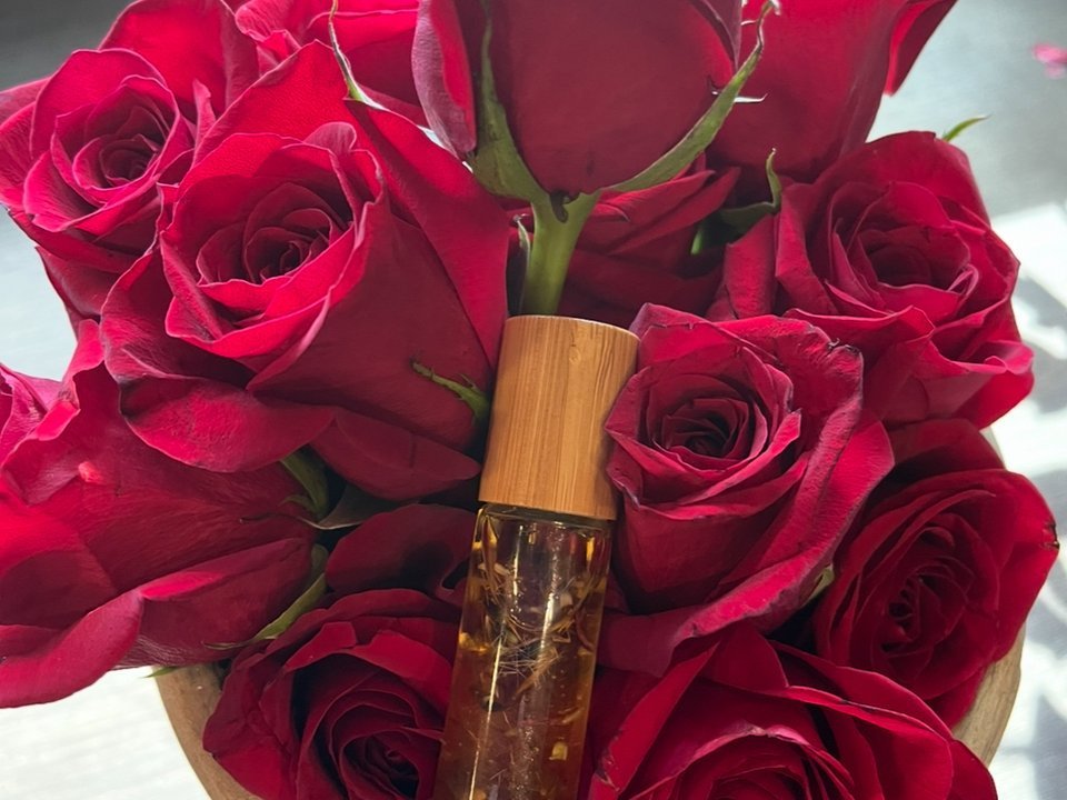A handcrafted fragrance oil roller bottle nestled among fresh red roses